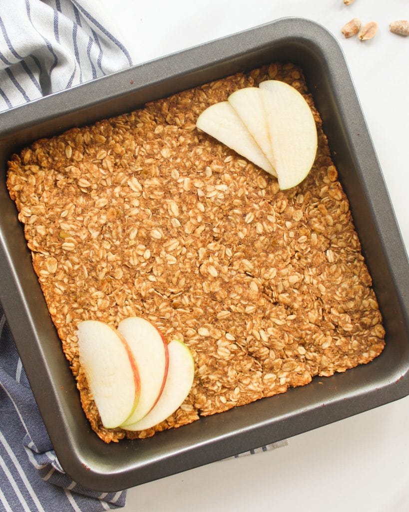 Baked oats in a black square baking pan with apple slices at the diagonals