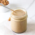 A side view pf almond butter in a jar with a spoon.