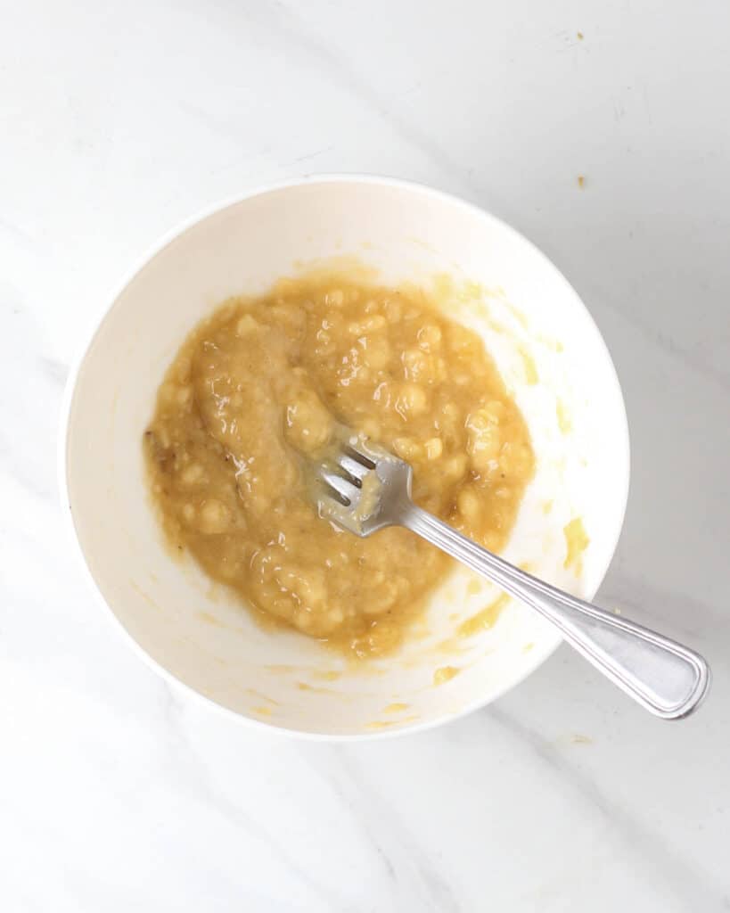 Mashed bananas in a white bowl with a fork.