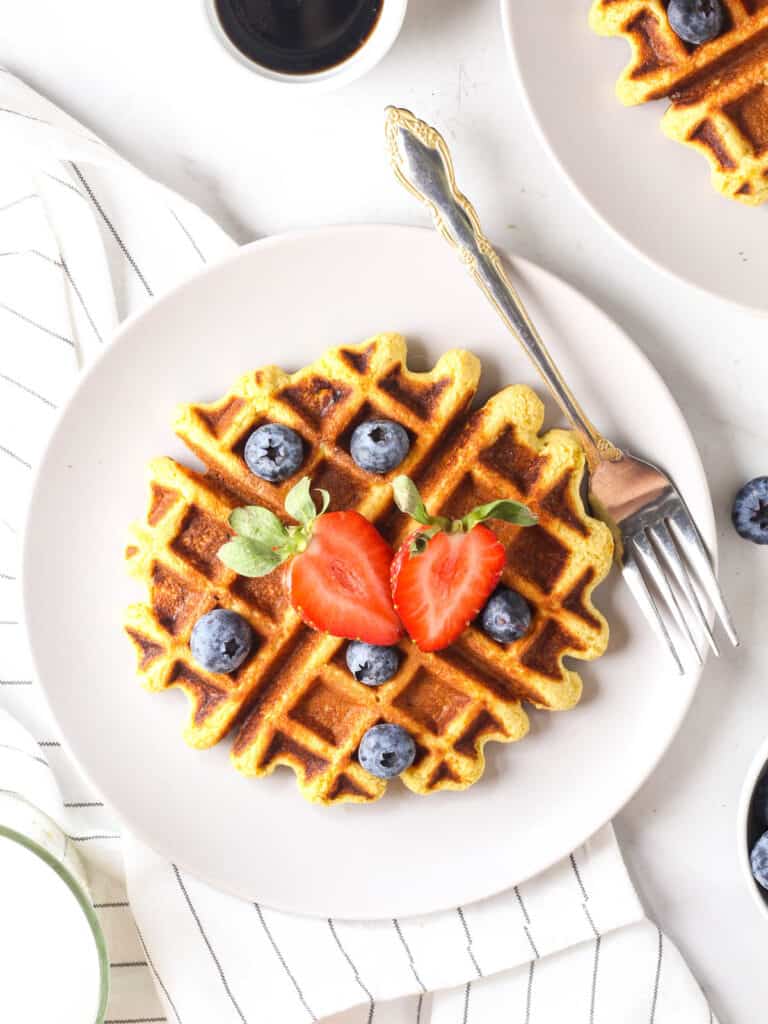 A piece of waffle served on a purple plate with a fork topped with fresh berries.