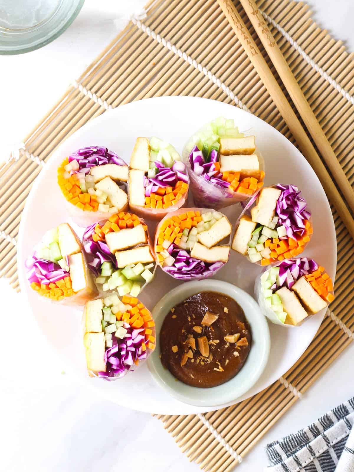 Rice paper rolls sliced into halves served on a white plate with a side of peanut sauce.