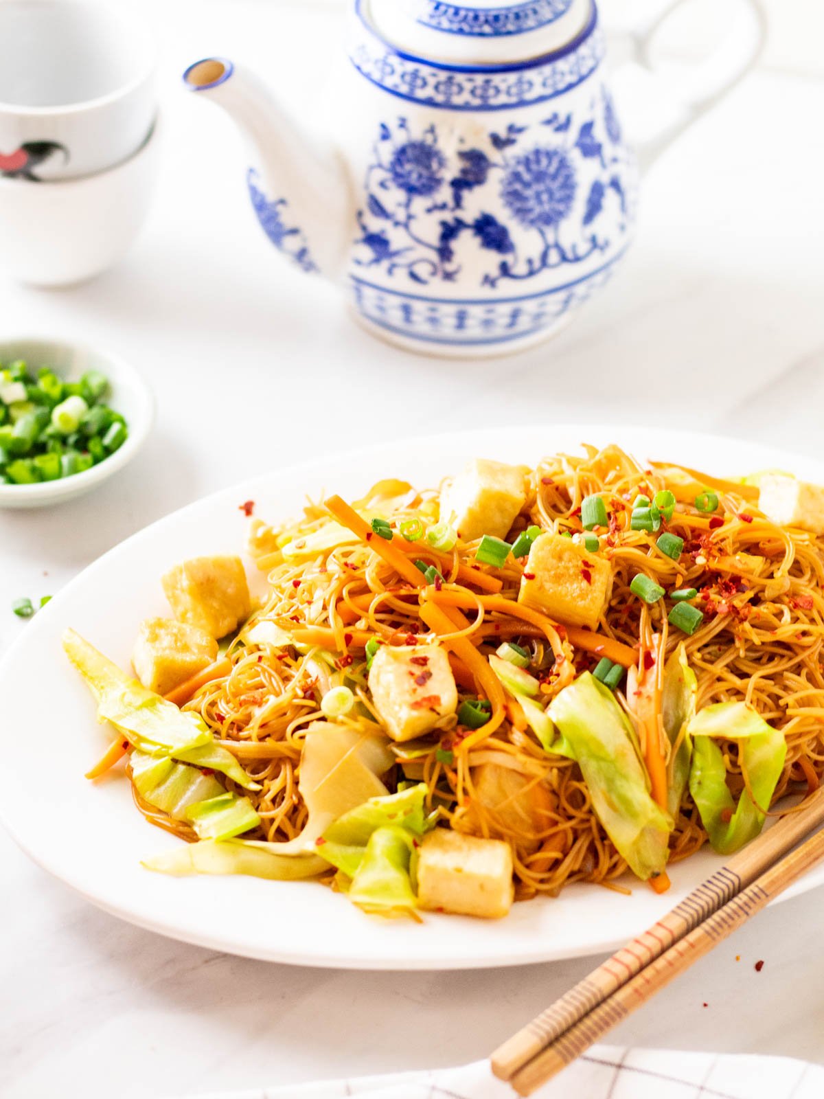 A head on shot of fried bee hoon served on a white oval plate with a pair of chopsticks at the side.