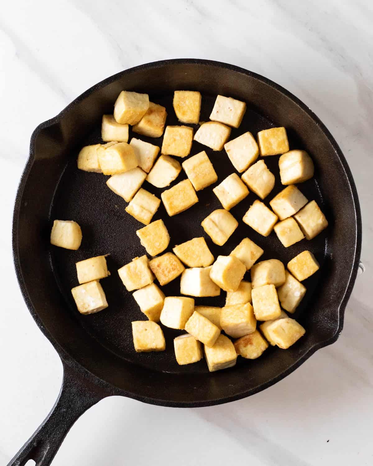 Pan frying tofu cubes in a cast iron pan.
