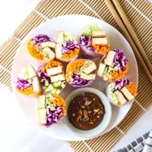 Summer rolls halves arranged on a plate served with peanut sauce.