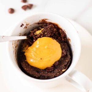 A close up shot of chocolate protein mug cake on a plate with a spoon.