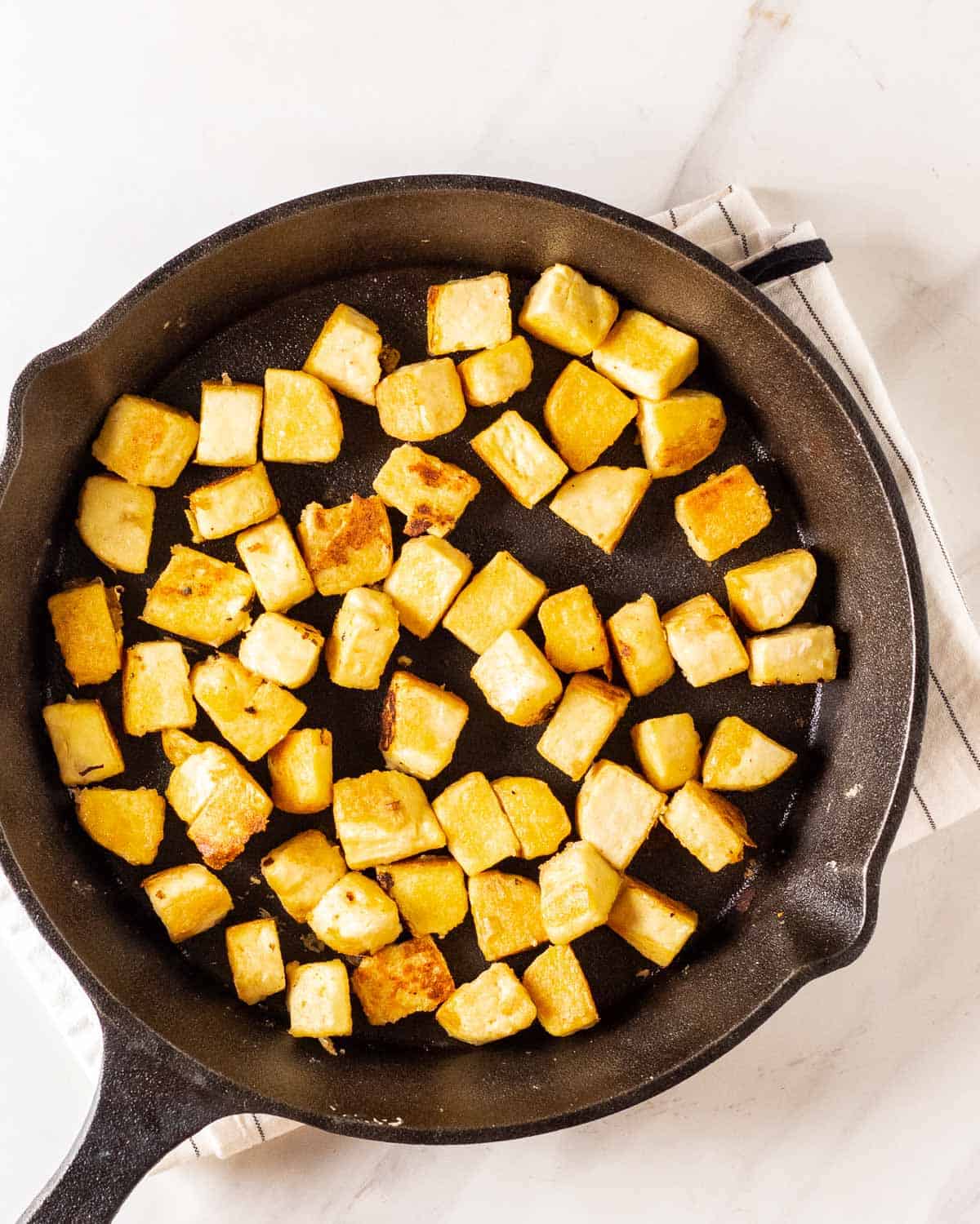 Pan fried tofu cubes in a cast iron pan.