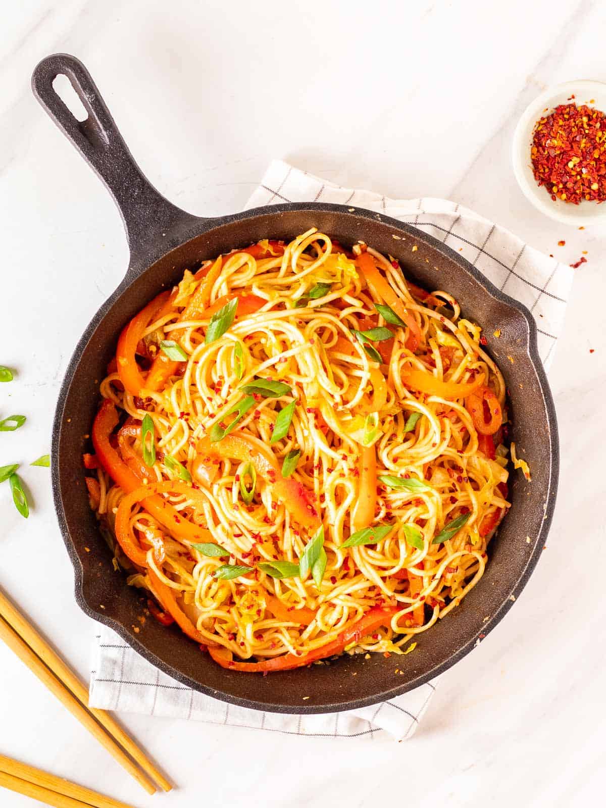 Gochujang noodles garnished with chopped green onions in a cast iron skillet.
