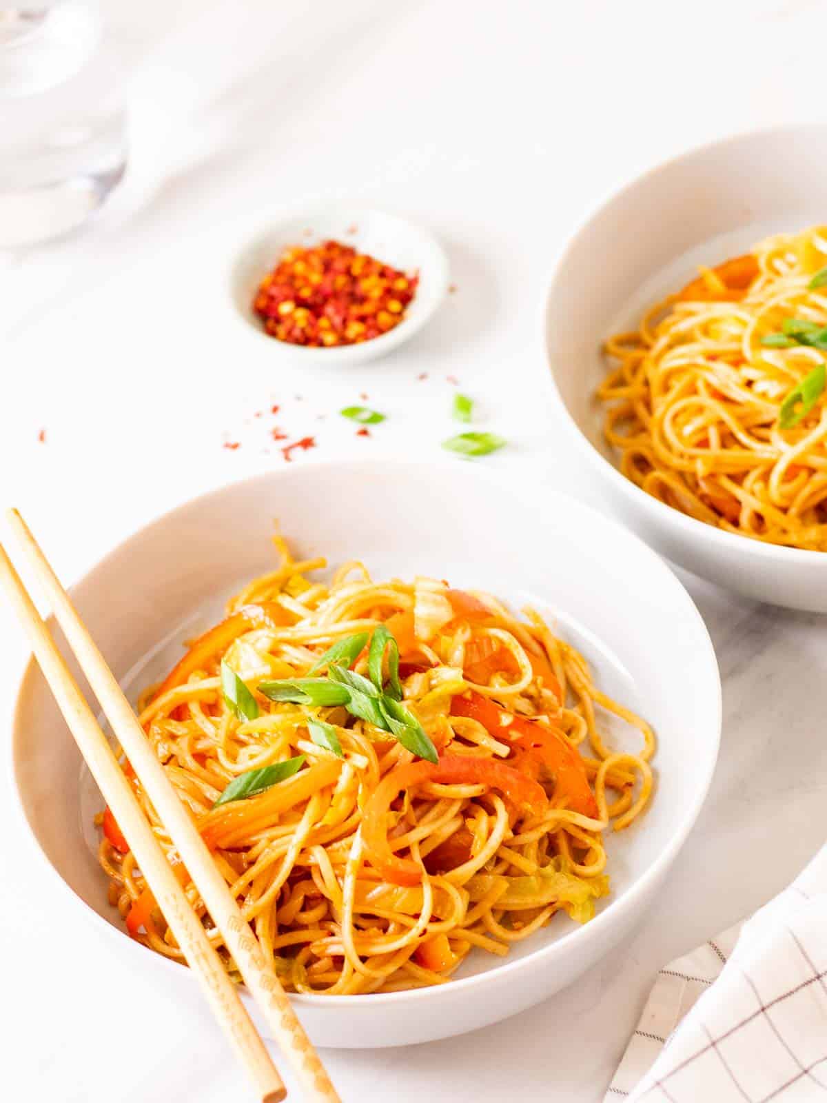 Gochujang noodles served in 2 deep plates topped with chopped green onion.