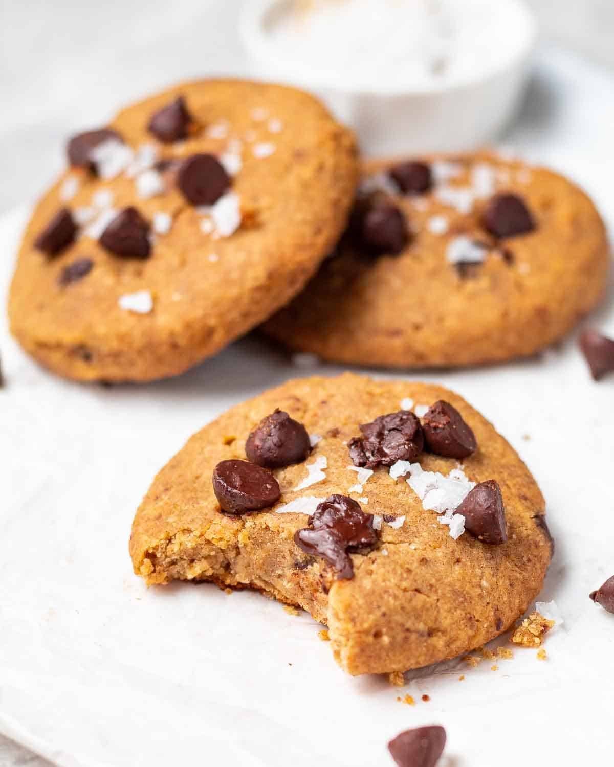A close up shot of a chickpea cookie with a bite taken out. There is another 2 cookies in the background.