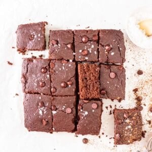 Slices of oat flour brownies arranged on a parchment paper with a small dish of flaked salt in the background.