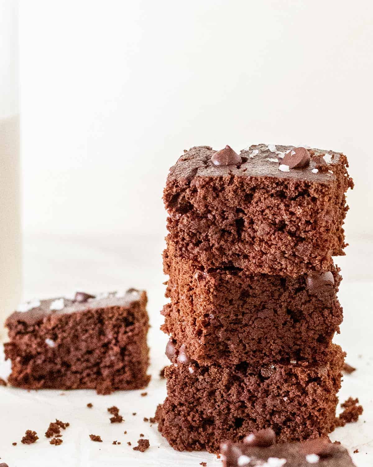 A stack of 3 brownies with a slice of brownie in the background.