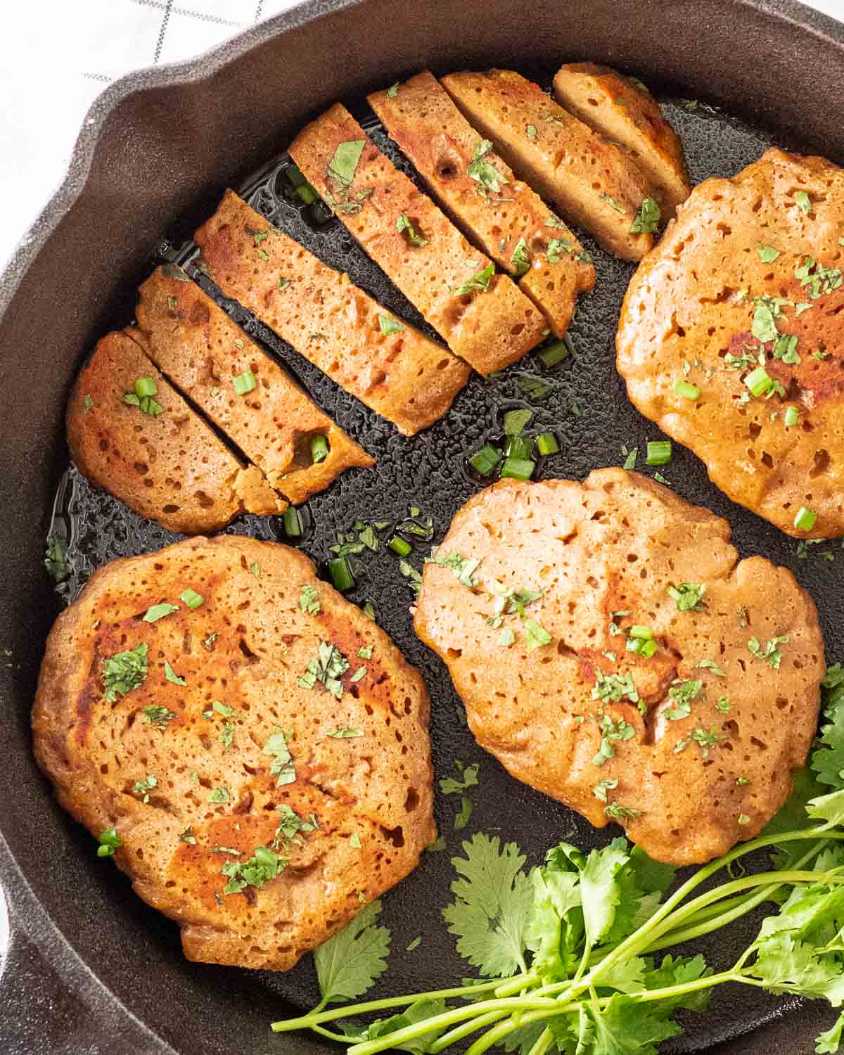 A few pieces of seitan chicken in a black pan with one of it being sliced into pieces. They are topped with chopped cilantro.