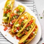 5 tacos arranged on a white oval plate.