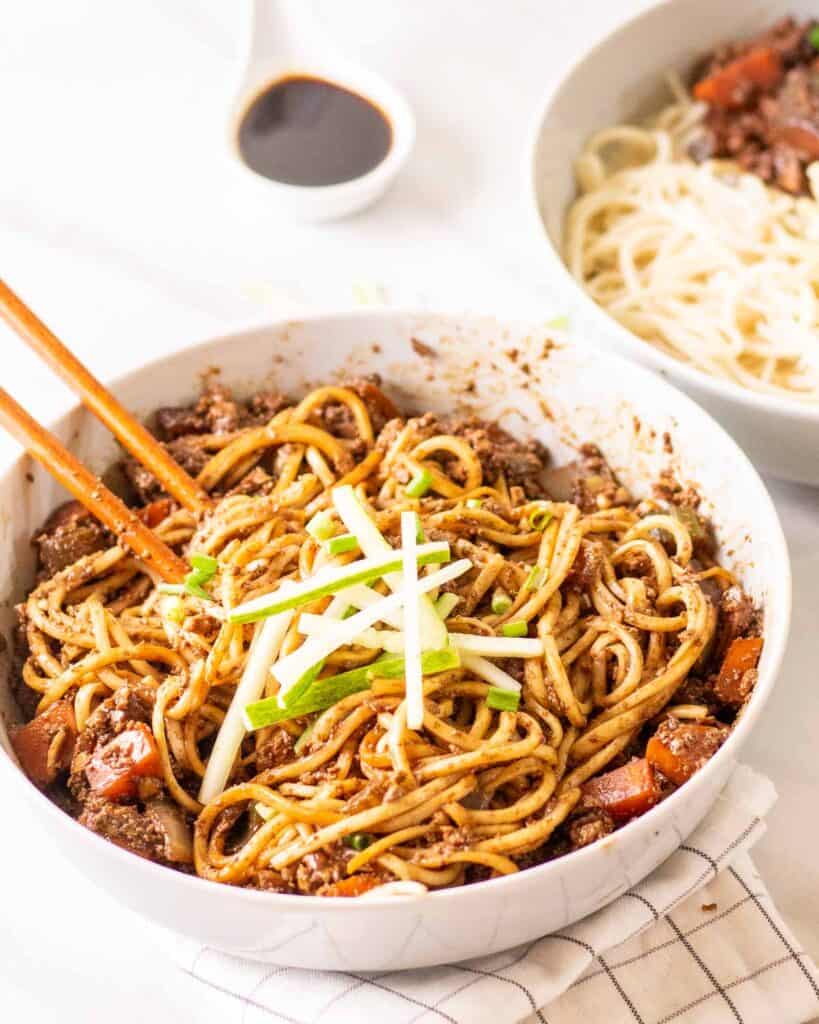 Bowl of noodles with sauce mixed in with chopsticks.