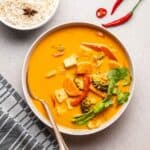 A close-up shot of curry served in a white bowl with a spoon on the side.