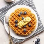 Waffles on a plate topped with banana slices and berries with a fork.