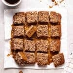 A tray of sliced coffee cake on parchment paper with a cup of coffee beside.