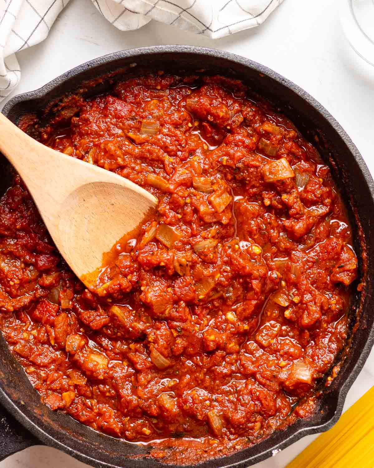 Marinara sauce in black pan with wooden stirrer.