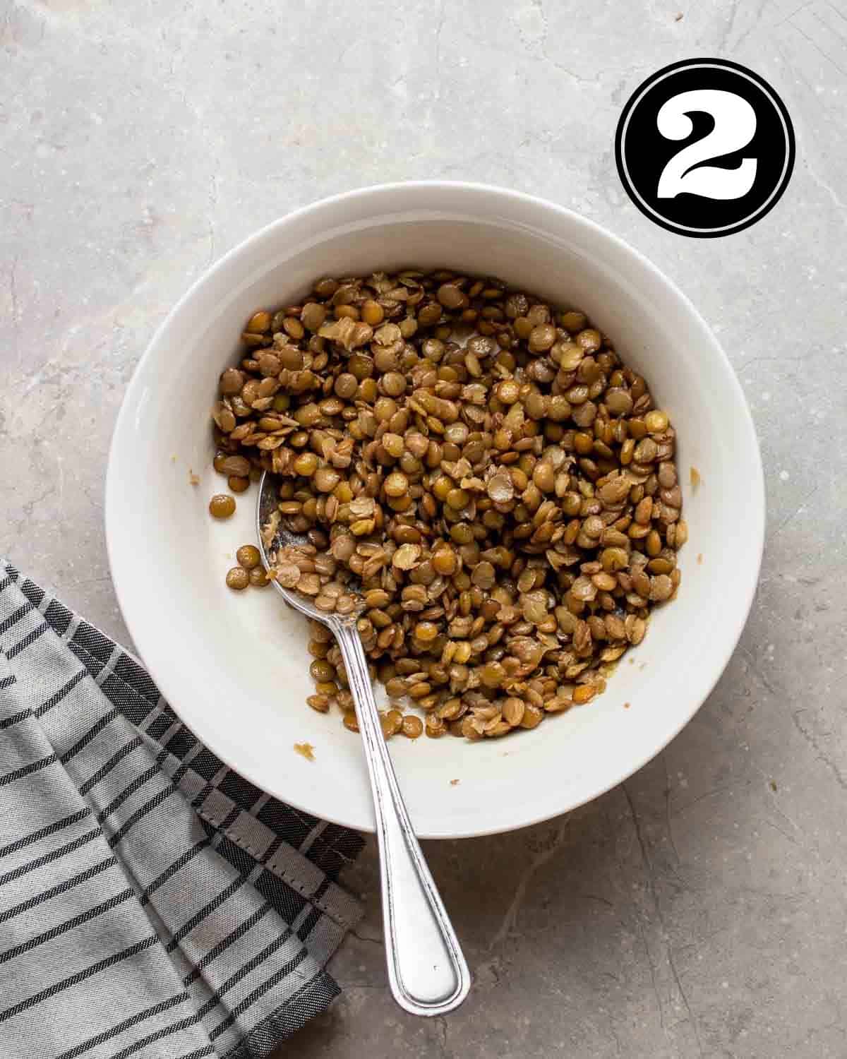 A bowl of seasoned lentils with a spoon beside.