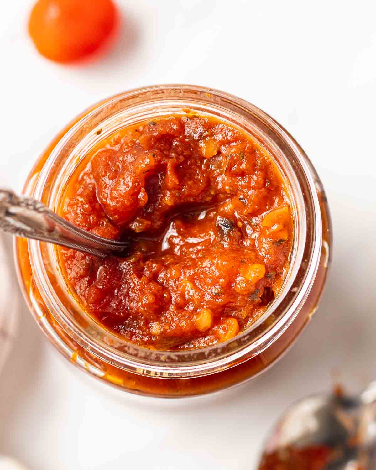Marinara sauce in glass jar with a spoon.