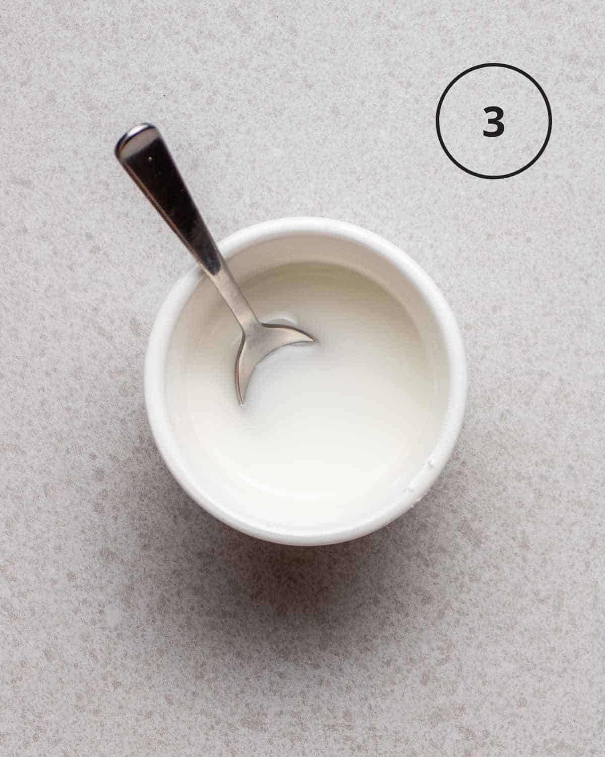 Cornstarch slurry in a white bowl with a spoon.