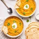 2 bowls of dal served with naan with spoons and more naan in the background.
