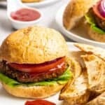 Black bean burger served with potato wedges with another burger and dish of tomato sauce behind.