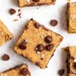 Few slices of blondies arranged on a parchment paper with chocolate chips in the background.
