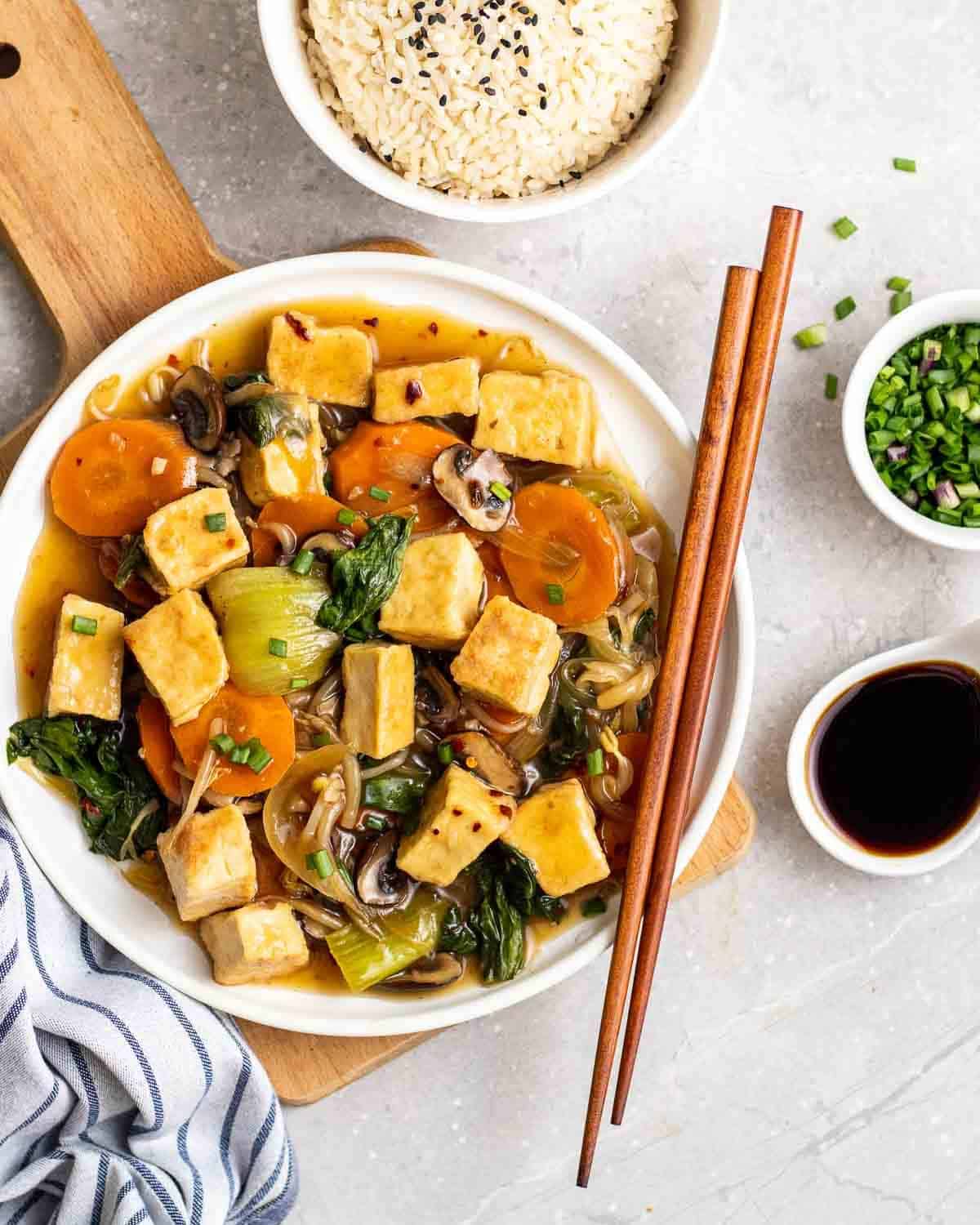 Chop suey in a white plate topped with chopped scallions with a chopstick.