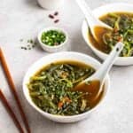 2 bowls of spinach soup topped with chopped scallions with spoons beside.