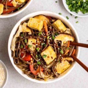 A bowl of yakisoba topped with chopped green onion and sesame seeds with chopsticks.