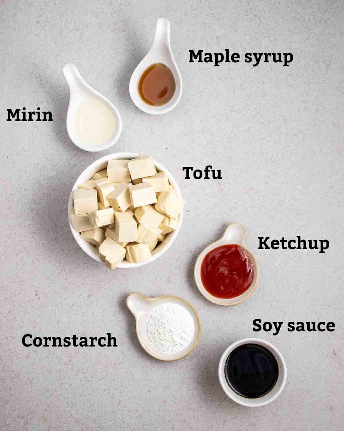 Ingredients needed like tofu, cornstarch, soy sauce and other seasonings on a grey background.