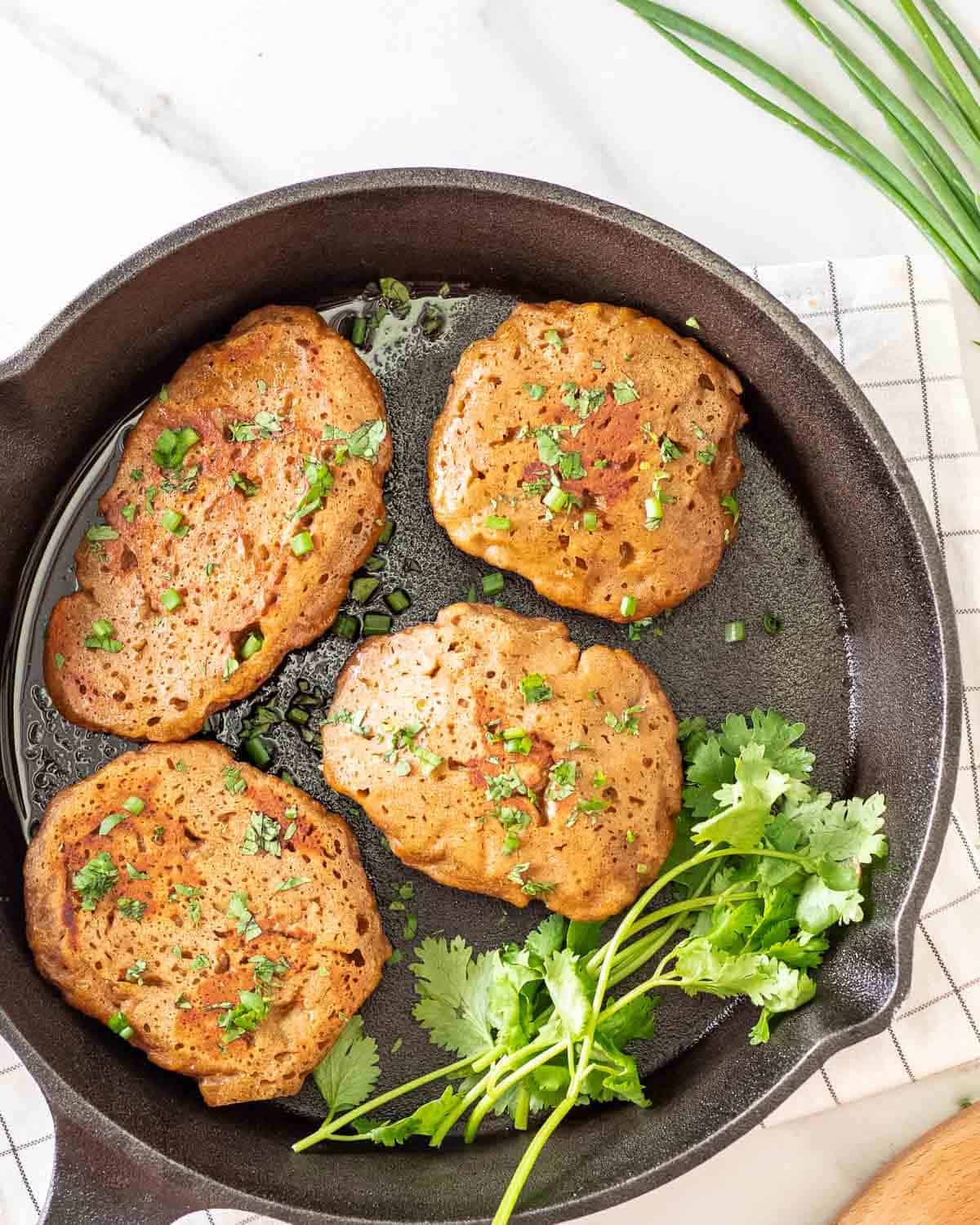 A few breast of seitan chicken in a cast iron skillet with stalks of parsley beside. 