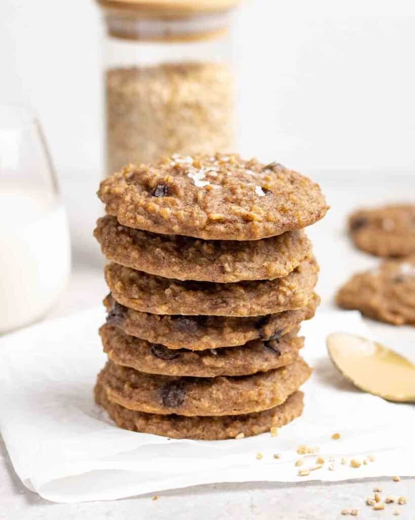 A stack of cookies with jar of steel cut oats, milk and spoonful of peanut butter behind.