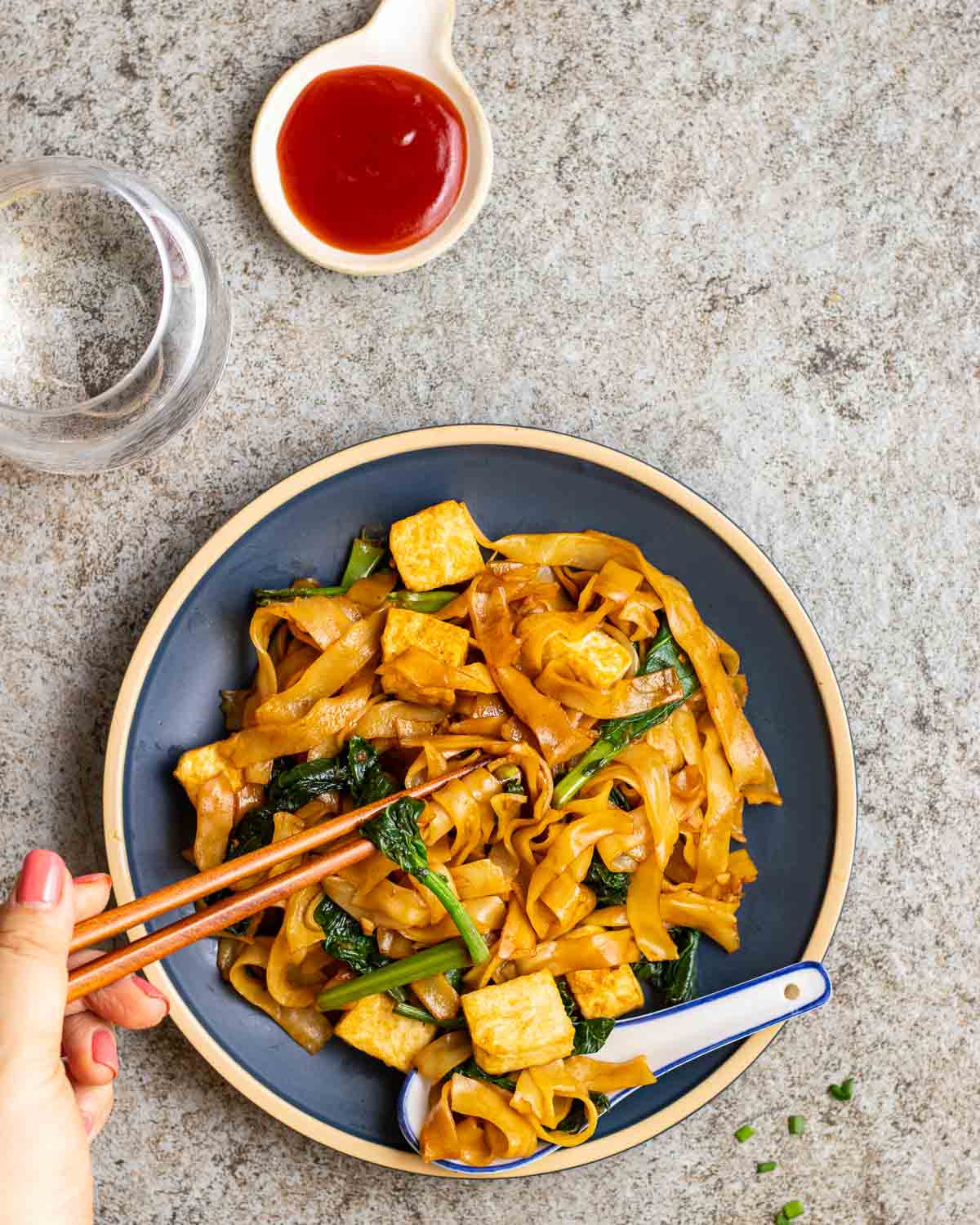 Taking out some noodles with a pair of wooden chopsticks from a blue plate.