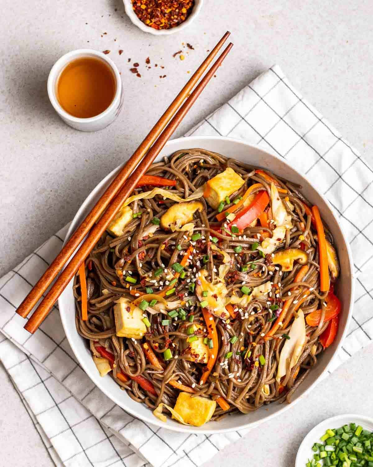 Noodles served in a deep plate with chopsticks and a cup of tea beside.