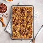 Baked oatmeal in glass dish with pecans, cinnamon sticks and a fork beside.