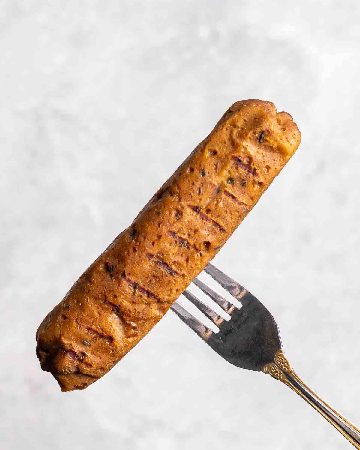 Fork holding a vegan Italian sausage on a grey background.
