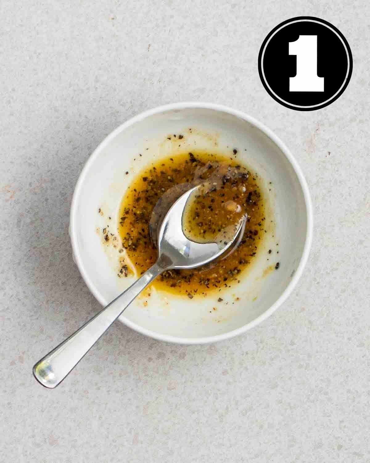 Marinade of mushrooms in a white bowl with a spoon beside.