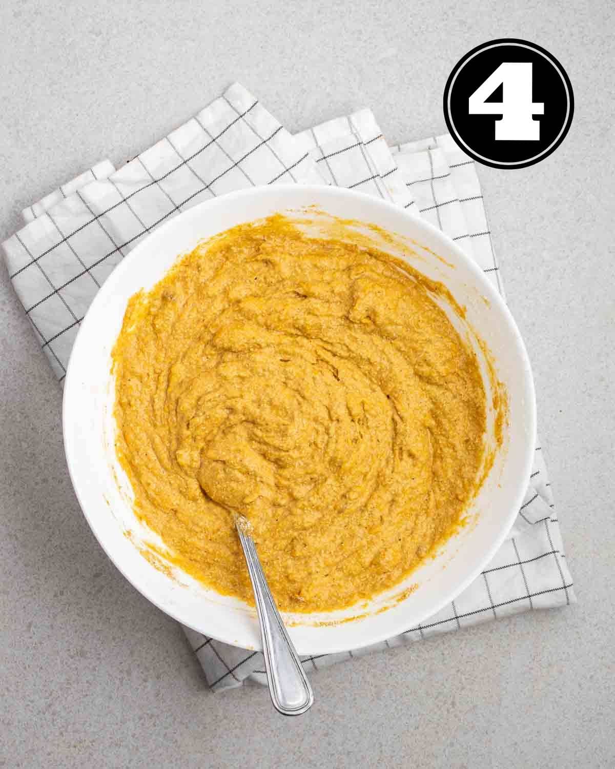 Batter of banana pumpkin bread in a large bowl with a fork beside on a white checkered teacloth.