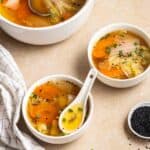 2 bowls of cabbage soup with dish of sesame seeds, teacloth and a pot beside.