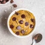 Mug cookie with a spoon and dish of chocolate chips beside.