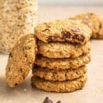 A stack of 5 oatmeal cookies with jar of oats and more cookies in the background.