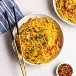 A plate of Singapore noodles topped with chopped green onions with a pair of chopsticks beside.