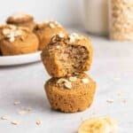 A stack of 2 muffins with plate of muffins, jar of milk and oats in the background.