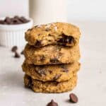 A stack of cookies with chocolate chips and jar of milk in the background.