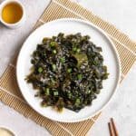 Seaweed salad on a plate on a bamboo sushi mat with a cup of tea beside.