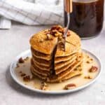 Stack of applesauce pancakes on a plate with a fork with jar of coffee in the background.