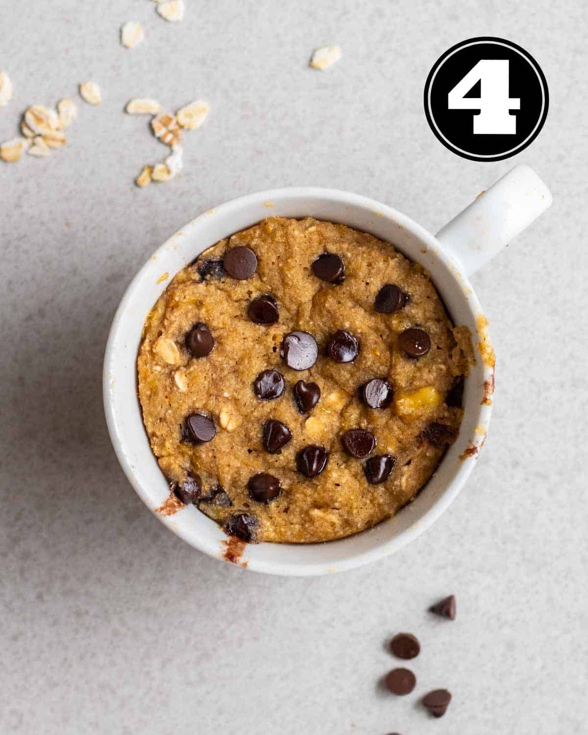 Cooked banana mug cake with oats and chocolate chips in the background.