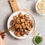 Plate of sambal eggplant with chopped green onion and bowl of rice beside.